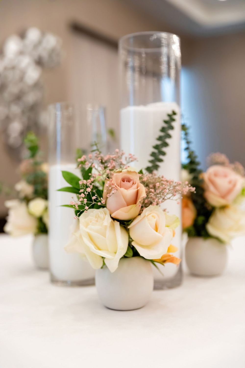 Delicate floral centerpieces with peach roses and white flowers in glass vases.
