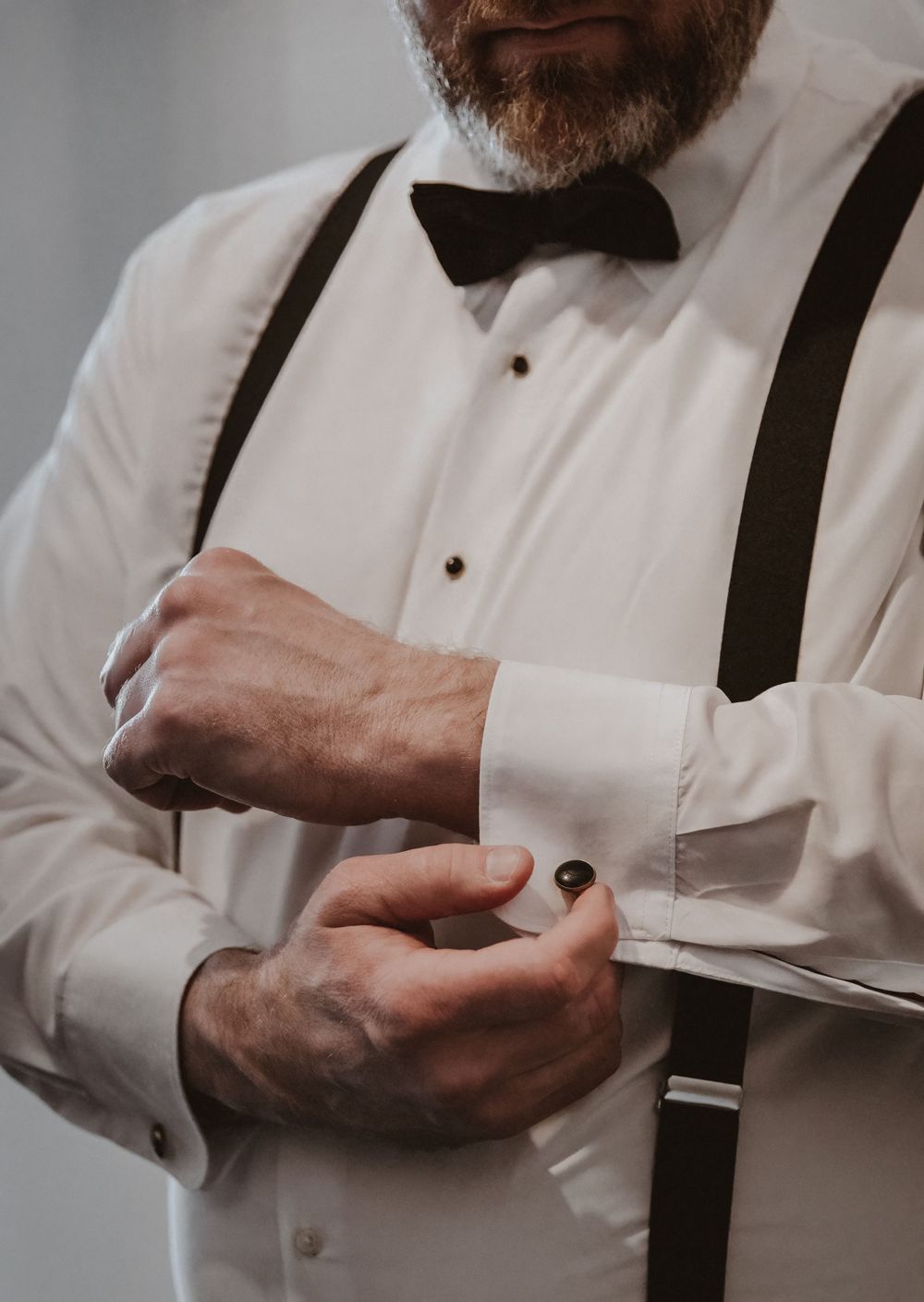 Close-up of formal white dress shirt with black suspenders being adjusted.