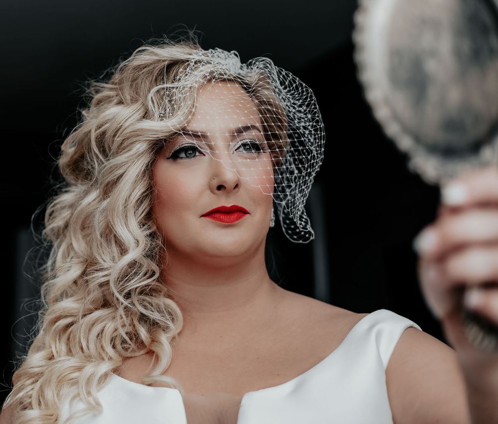 Bridal portrait with vintage-style birdcage veil and bold red lipstick.