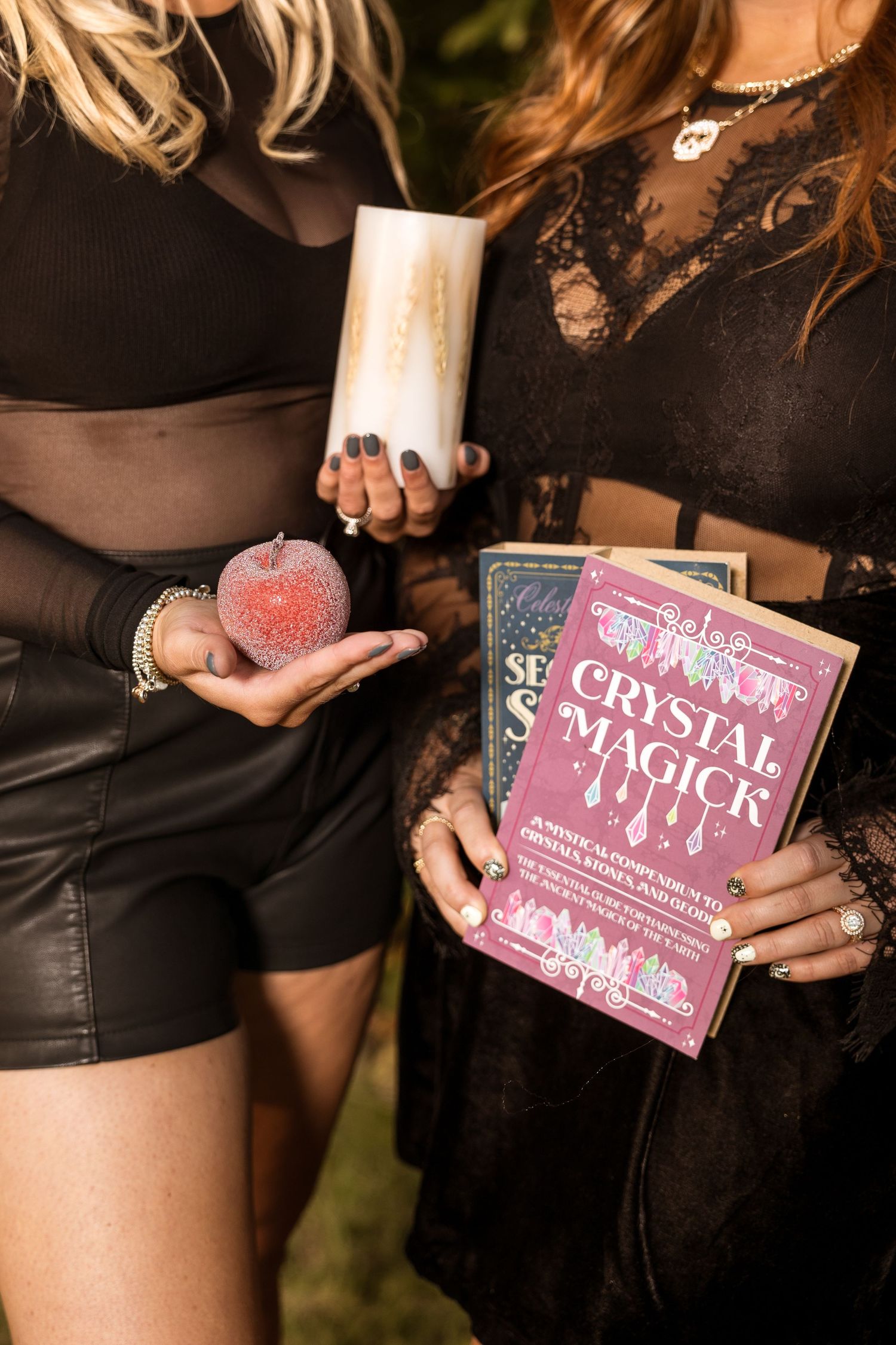 Two people in black gothic attire hold crystal magic books and mystical items at a Halloween gathering.