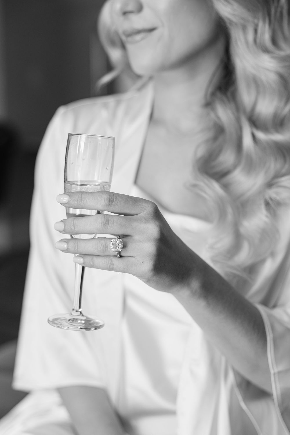 Hand holding champagne glass shows off engagement ring in black and white photo.