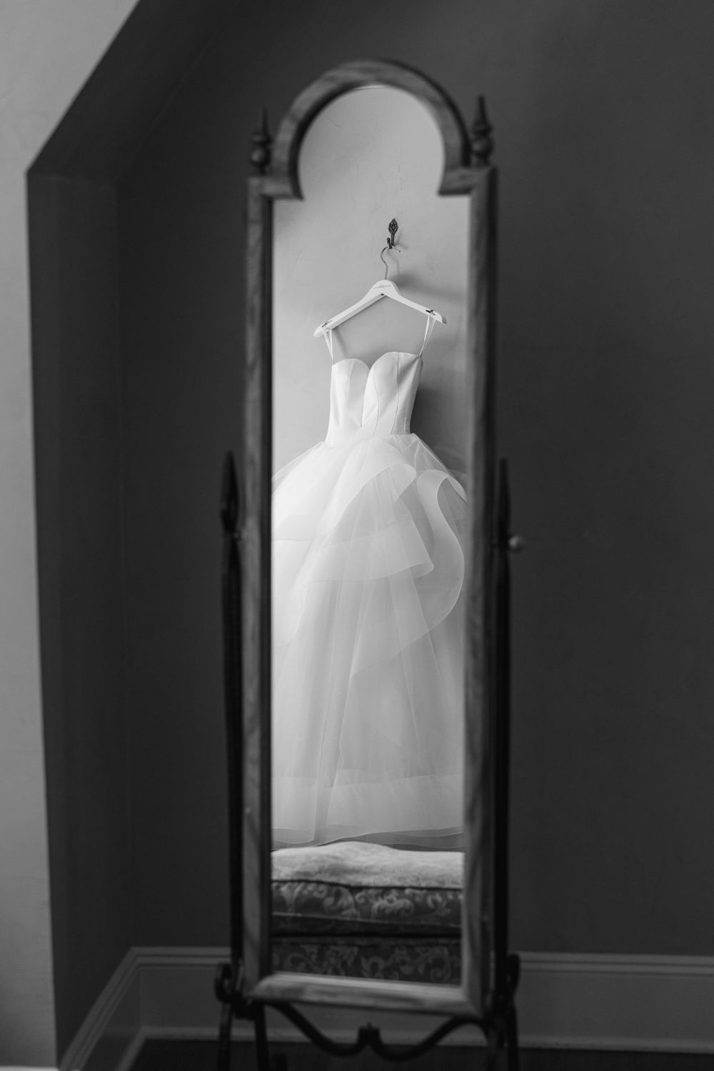 White wedding dress hanging in vintage full-length mirror creates dramatic silhouette.