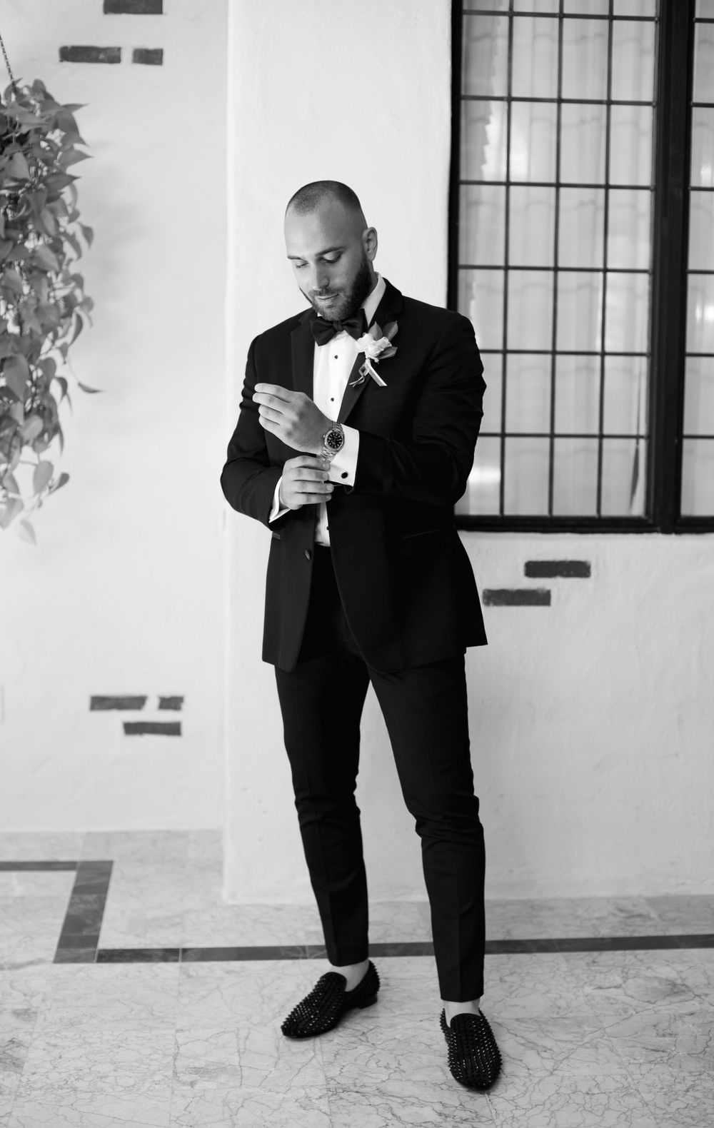 Groom in black tuxedo adjusts cufflinks before ceremony.