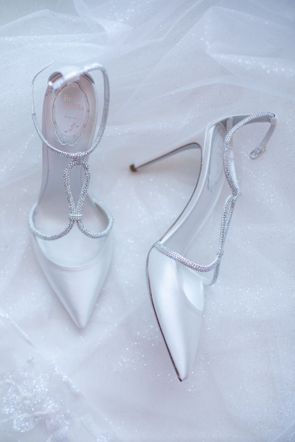 Elegant white bridal shoes with crystal embellishments on tulle fabric.