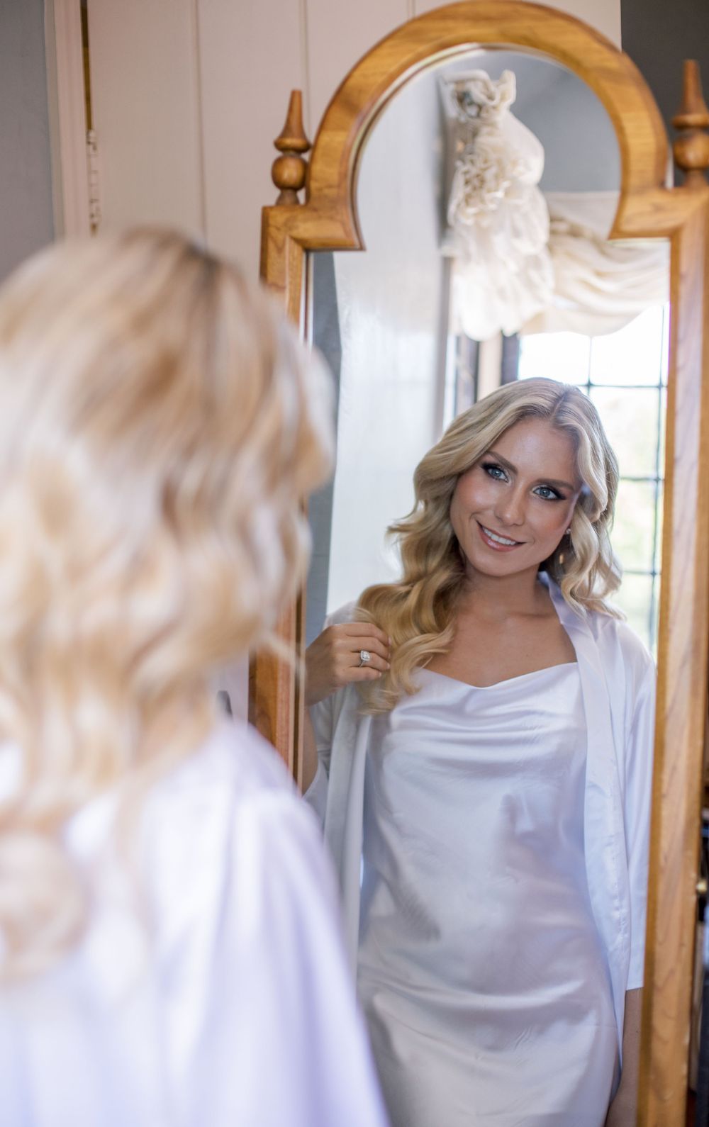 Reflection of a woman in a white robe looking at herself in an ornate gold mirror.
