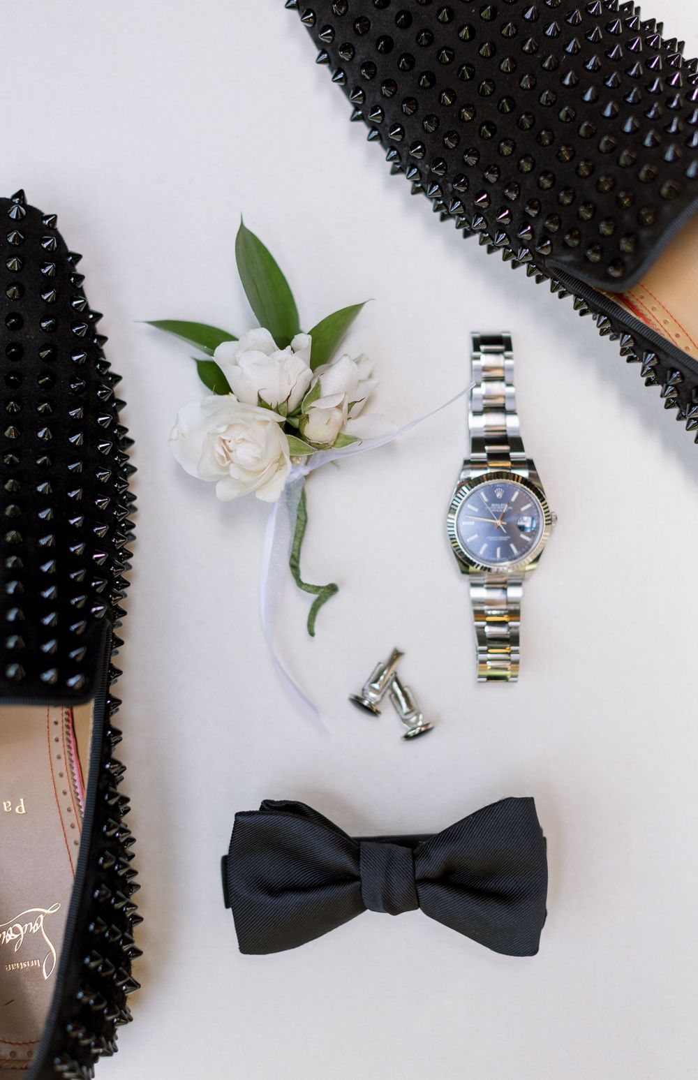 Wedding accessories flatlay with spiked loafers, boutonniere, watch and black bowtie.
