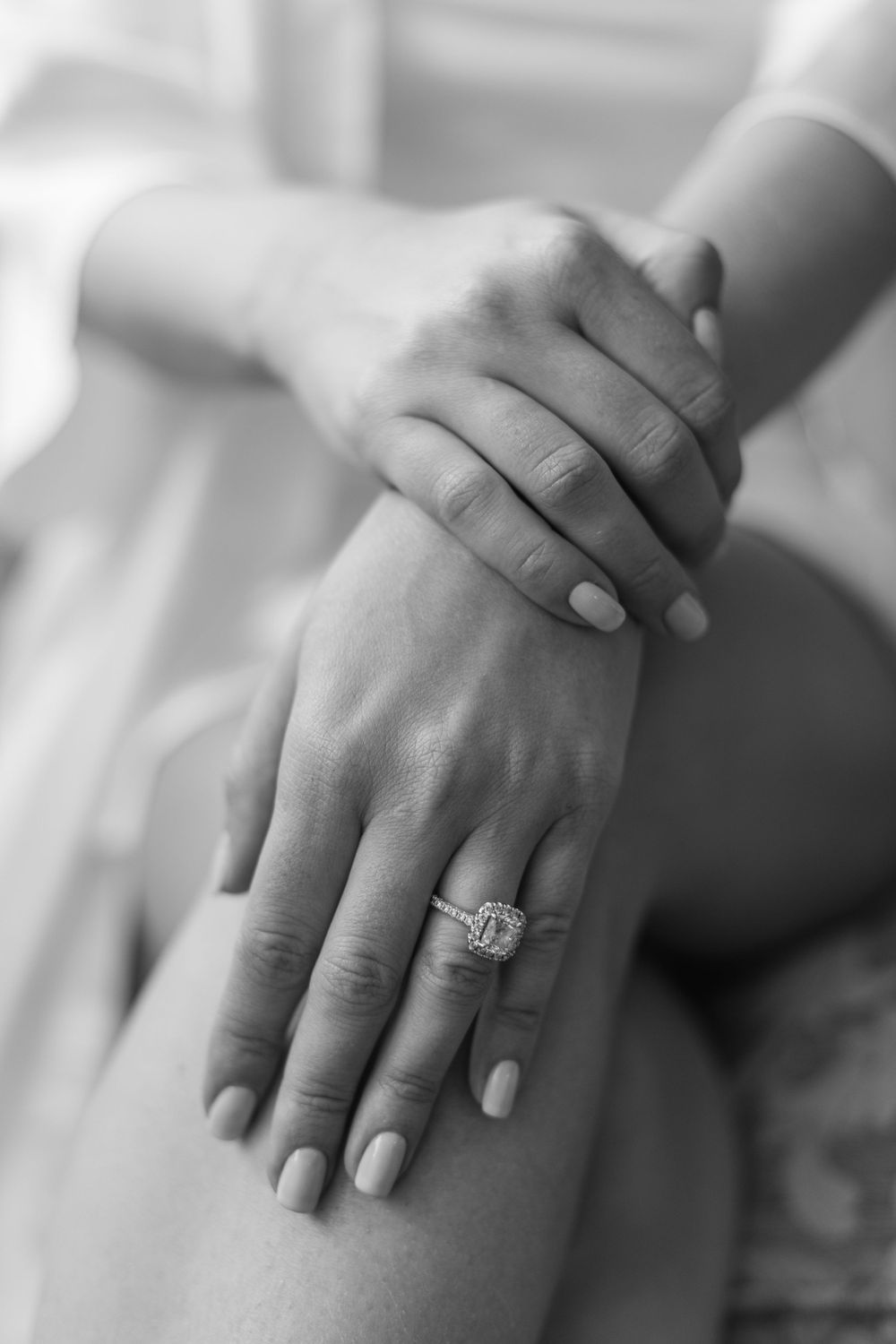 Close-up of hands displaying an engagement ring with neutral manicure.