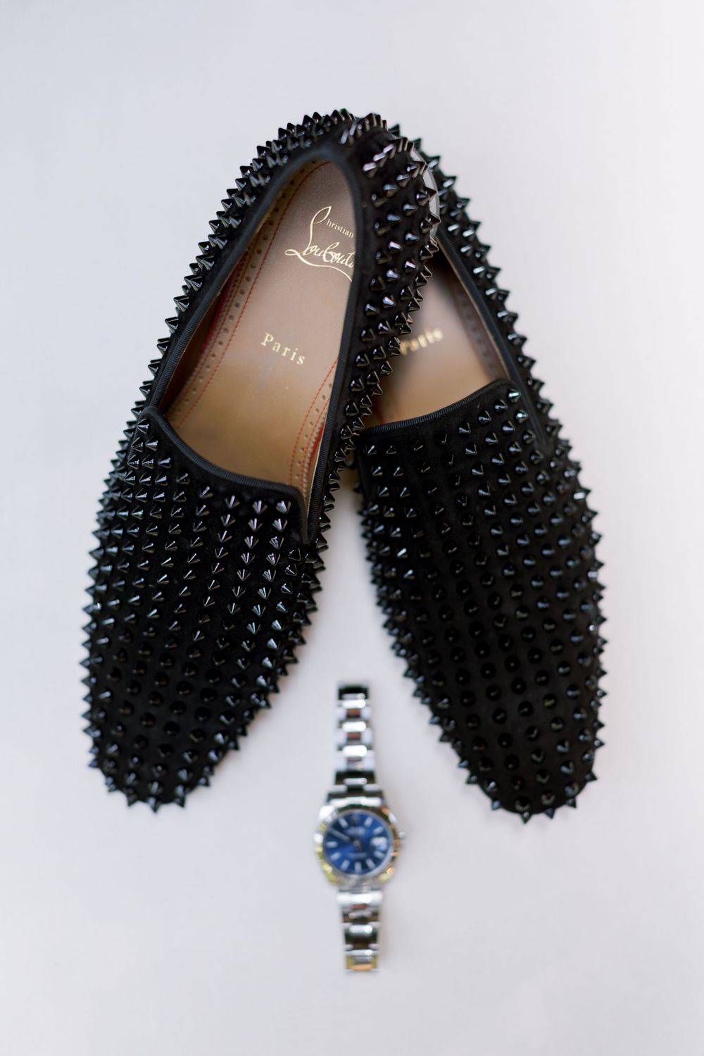 Black studded loafers and silver watch arranged on white background.
