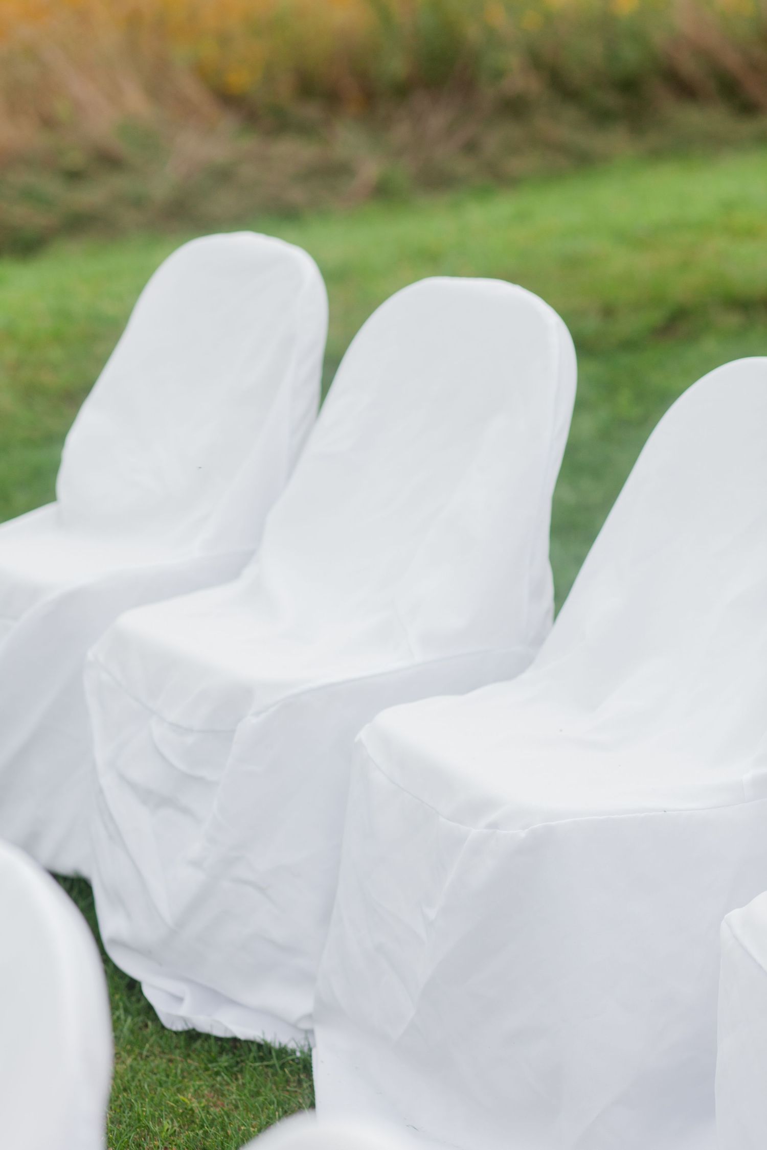 White folding chairs with covers set up for an outdoor wedding ceremony on green grass.