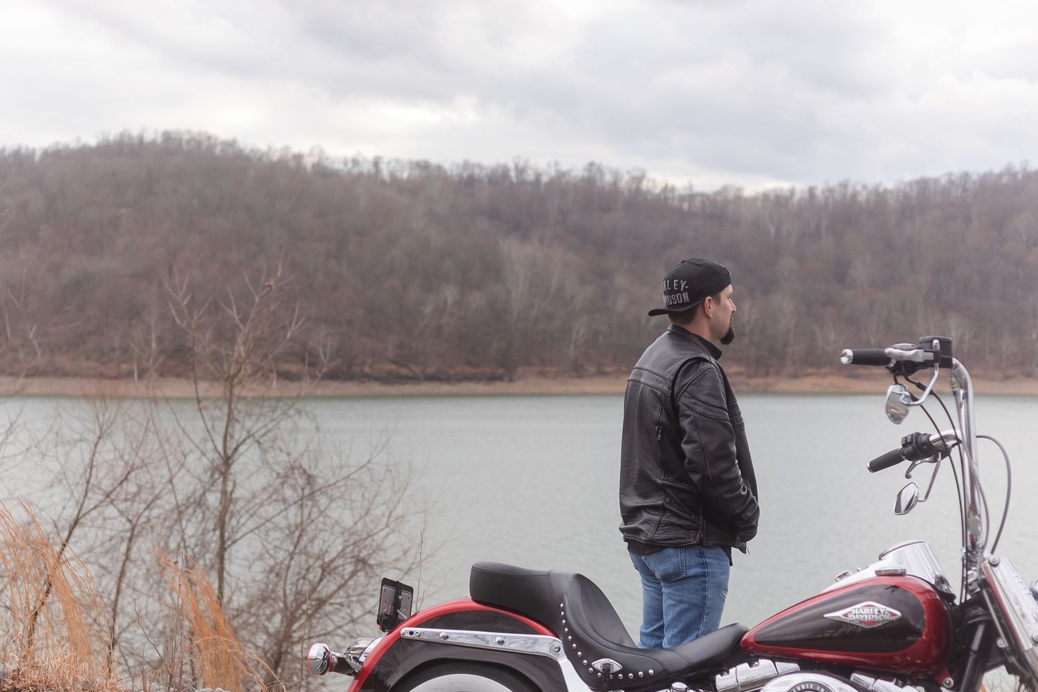 A motorcycle is parked by a lake with hills in the background on a cloudy day.
