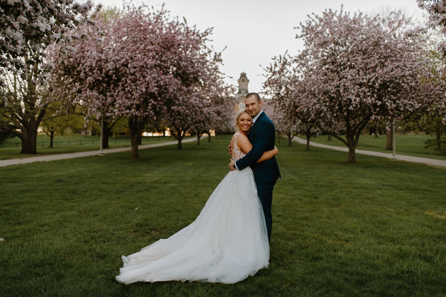 A wedding couple poses in a spring garden with blooming cherry trees.