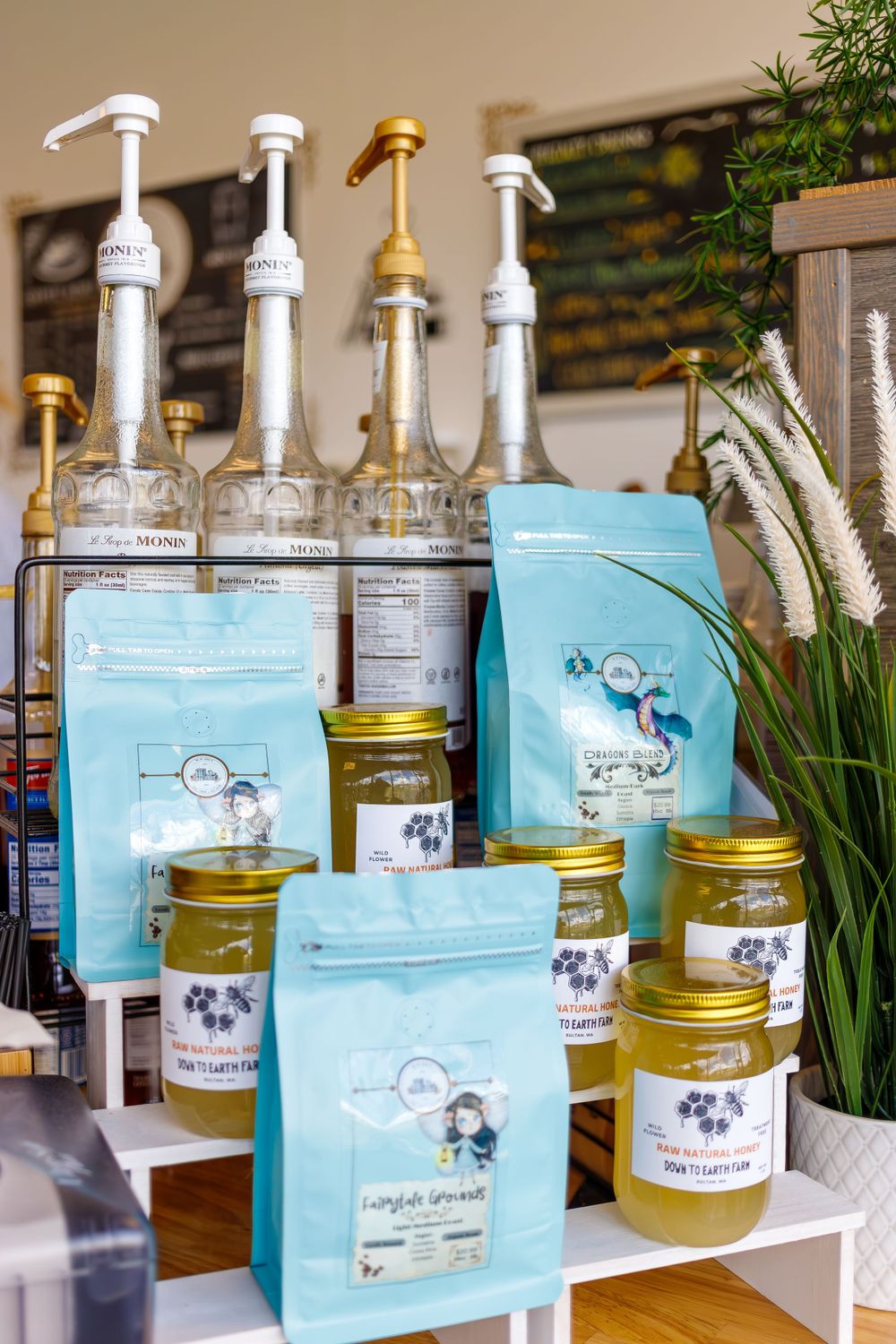 Coffee syrups and retail coffee bags displayed with decorative plants.