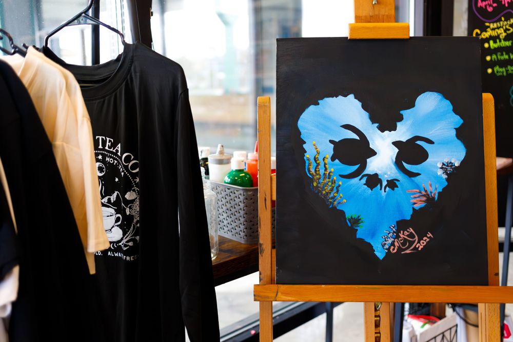 Retail display featuring black clothing and blue artwork on an easel.