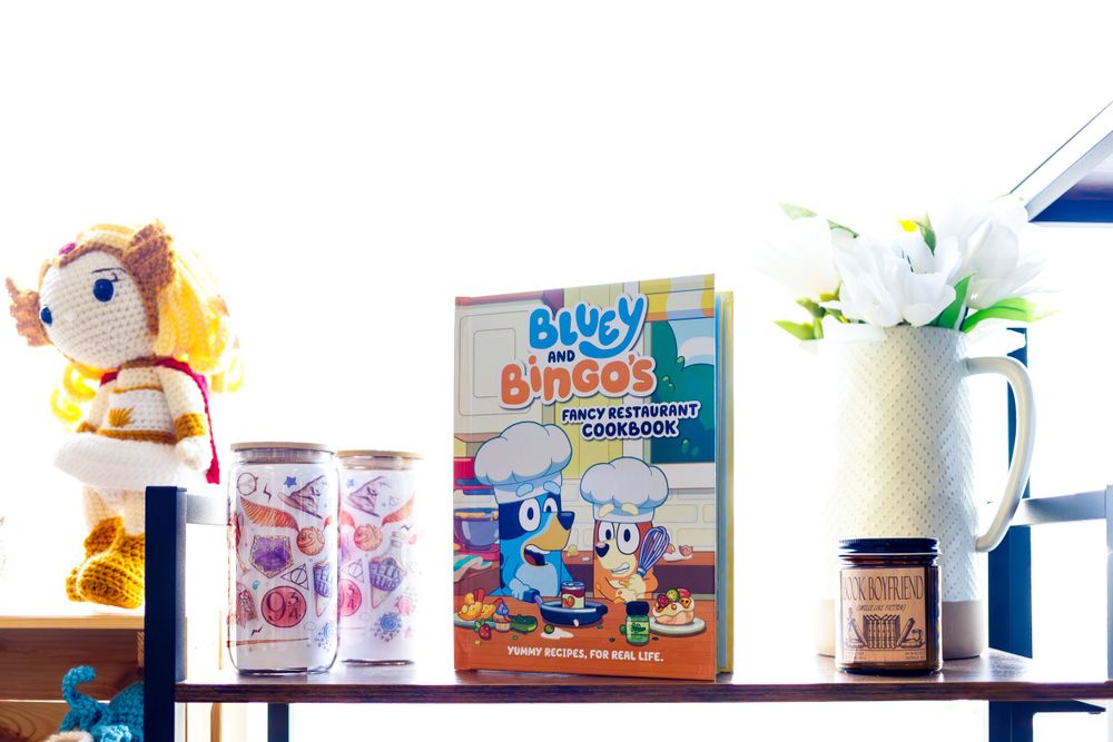 Bluey merchandise and plush toys displayed on wooden shelf with a vase of flowers.