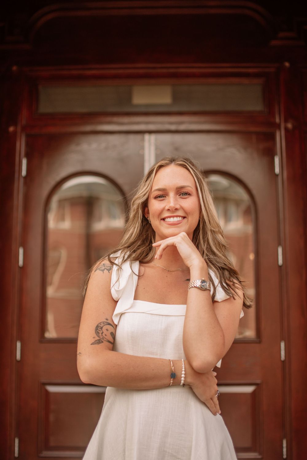 Portrait in front of ornate wooden university doors showing graduation celebration.