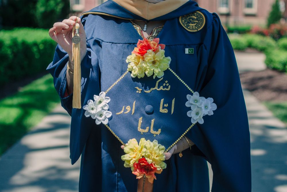 Decorated graduation cap with Arabic text and colorful flowers against blue gown.