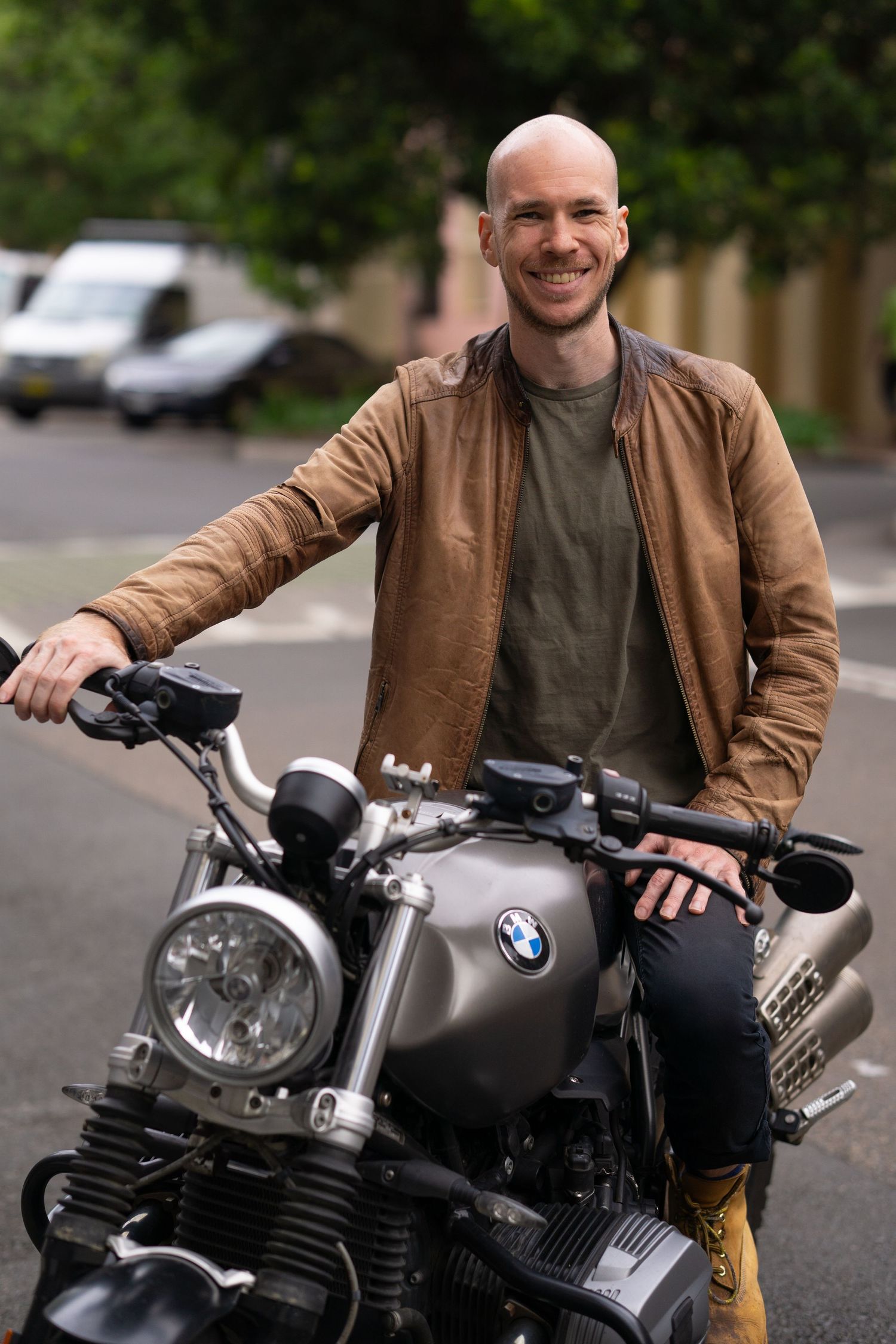 Casual man in brown jacket smiles while sitting on parked BMW motorcycle.