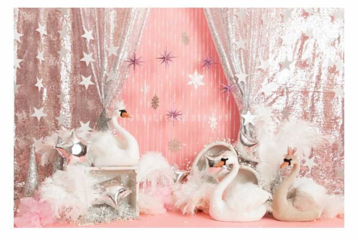 Whimsical winter holiday display with white swans, sparkly stars and pink background against snowy forest scene.
