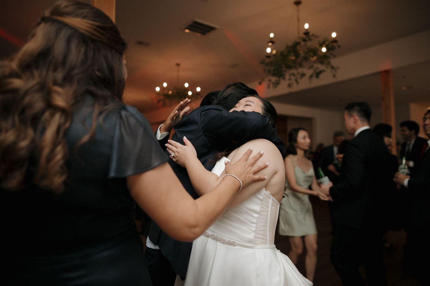 Guests sharing an emotional embrace during a wedding reception under chandelier lighting.