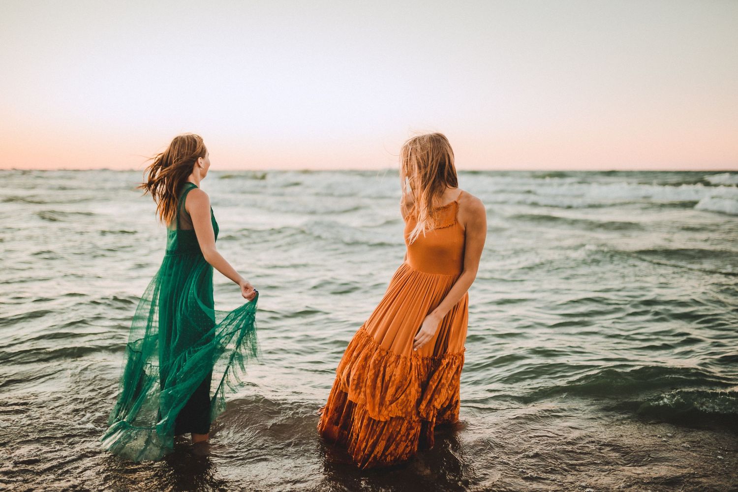 Friends in colorful maxi dresses enjoying the waves at sunset.