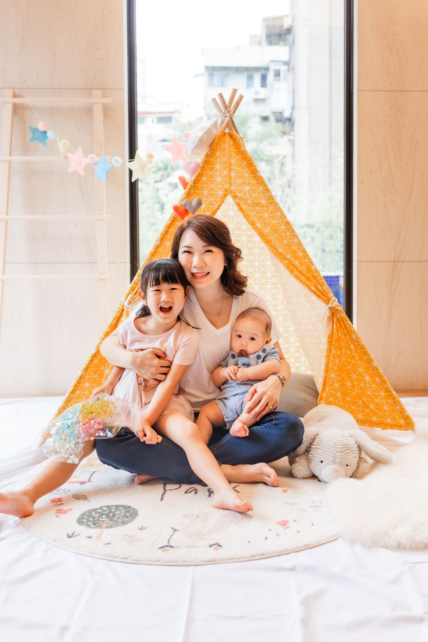 Family sitting together in front of an orange teepee tent with decorative string lights.