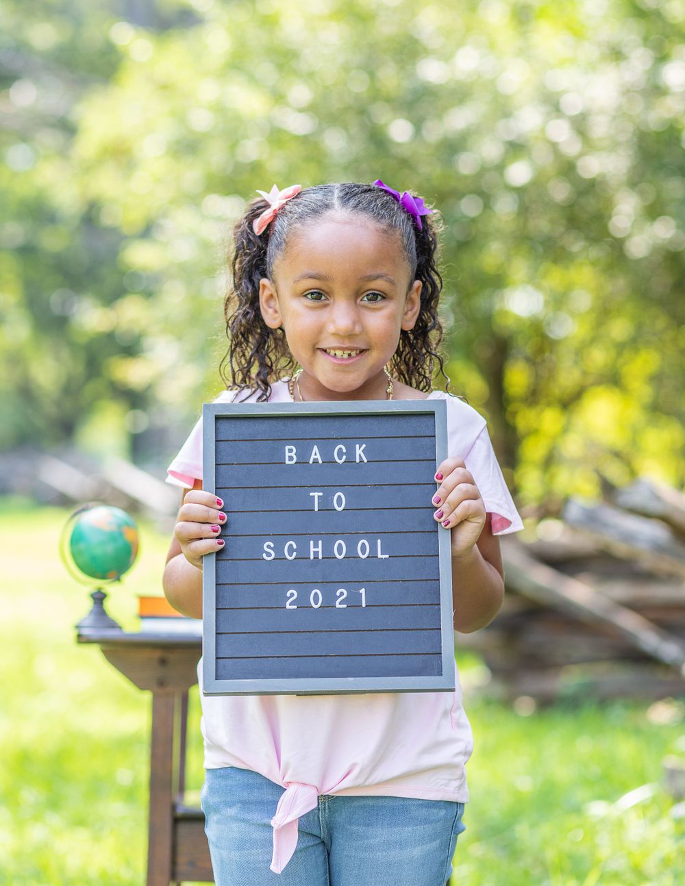 Student displays a gray letterboard with 'Back to School 2021' message next to small decorative globe.