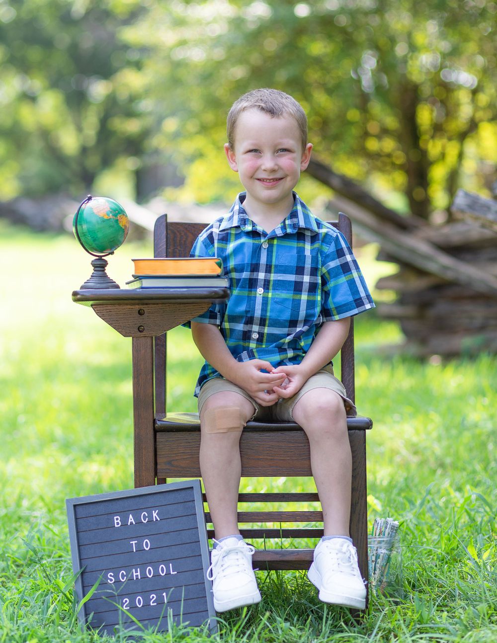 Student sits on wooden chair outdoors with school supplies and a 'Back to School 2021' sign.