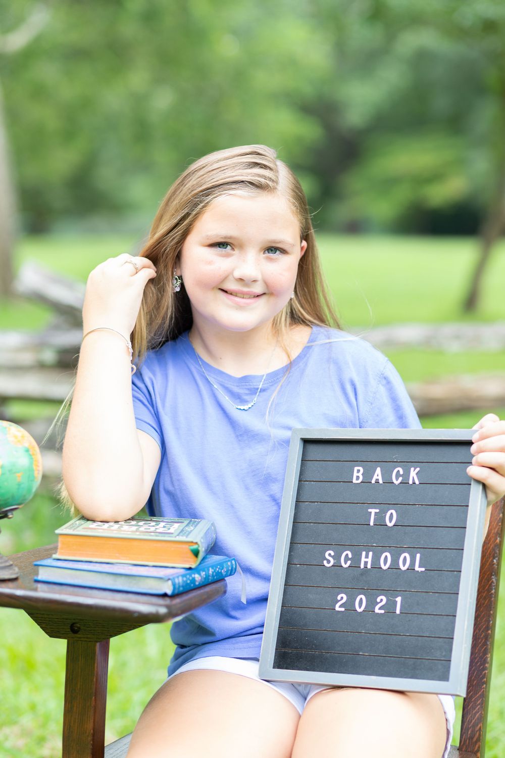 Student in blue shirt holds letterboard sign while sitting outdoors with globe and books.