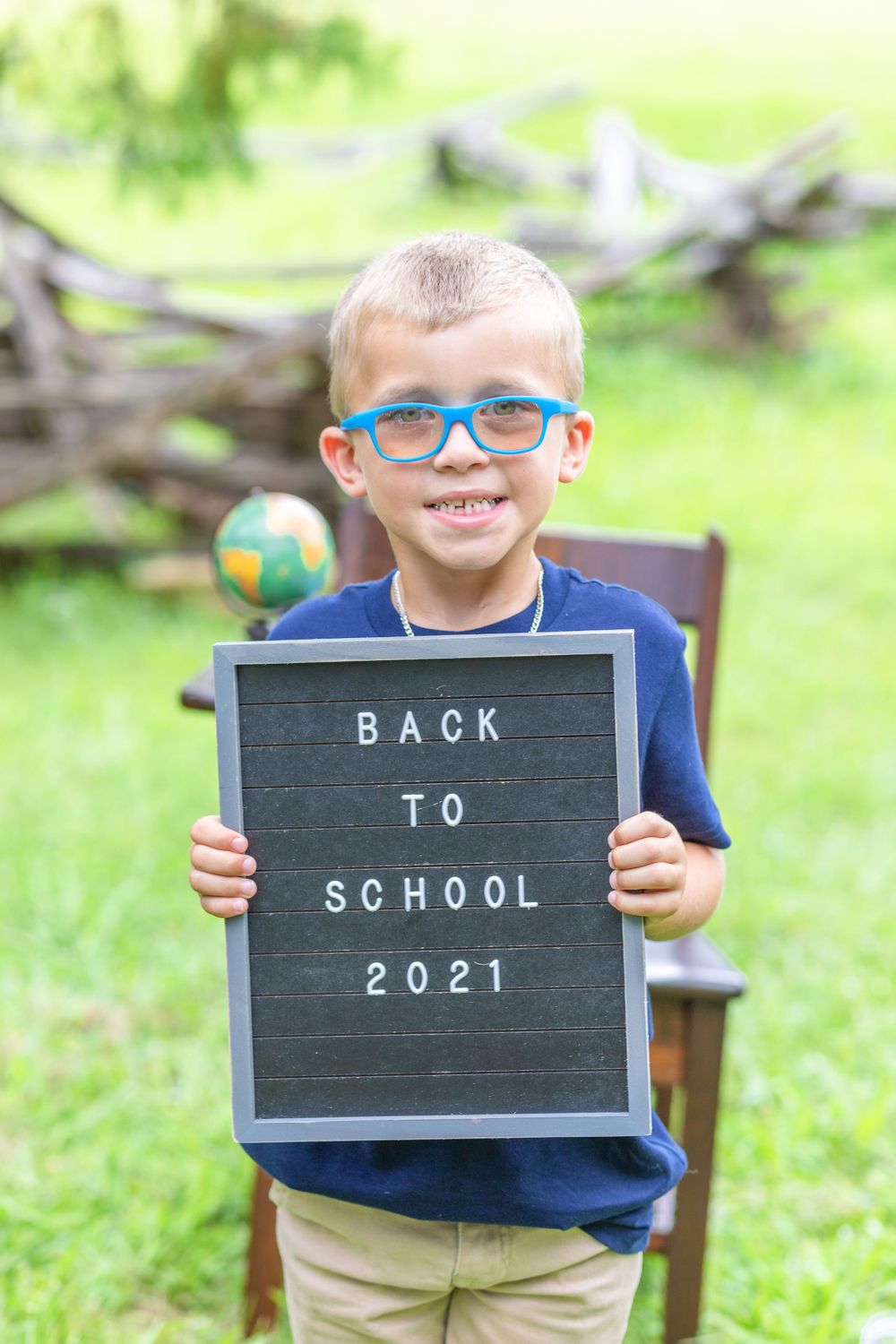 Student wearing blue glasses holds gray letterboard with back-to-school message outdoors.