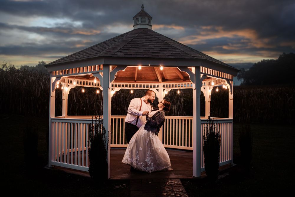 Couple shares romantic moment in lit gazebo during twilight wedding photoshoot.