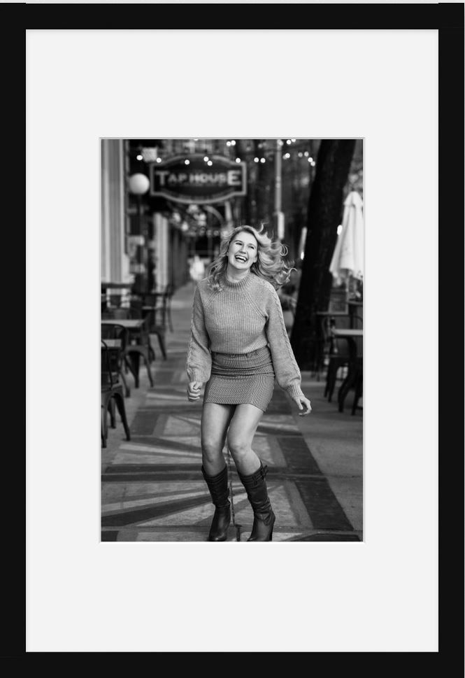 A black and white street photo showing a figure in a sweater and boots walking outdoors.