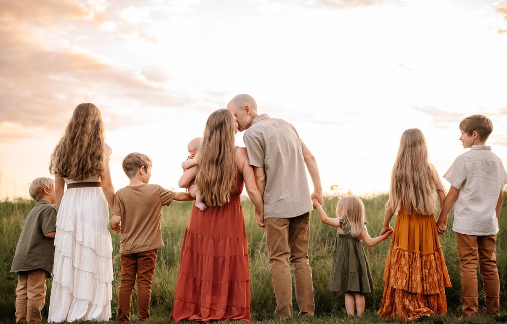 Family in flowing dresses holding hands while walking at sunset in field.