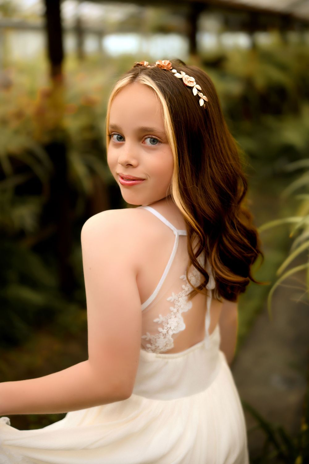 A portrait in a greenhouse featuring a white dress with delicate lace details.