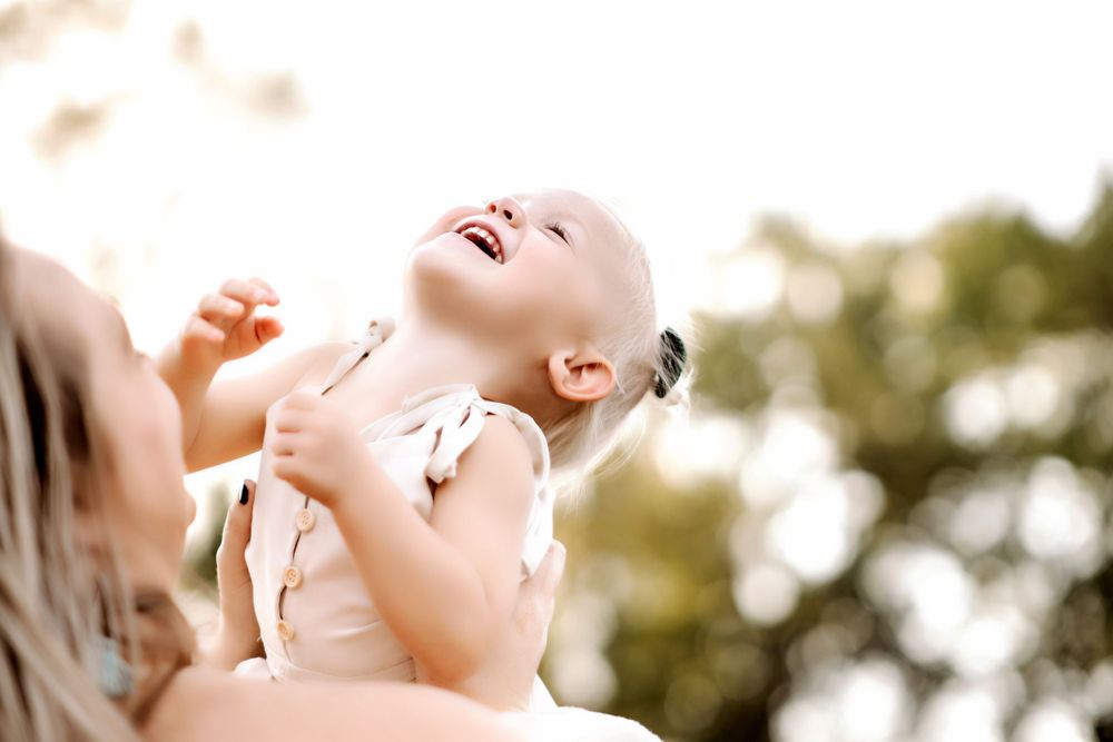 Candid shot of joyful toddler being lifted in the air during sunset photoshoot.