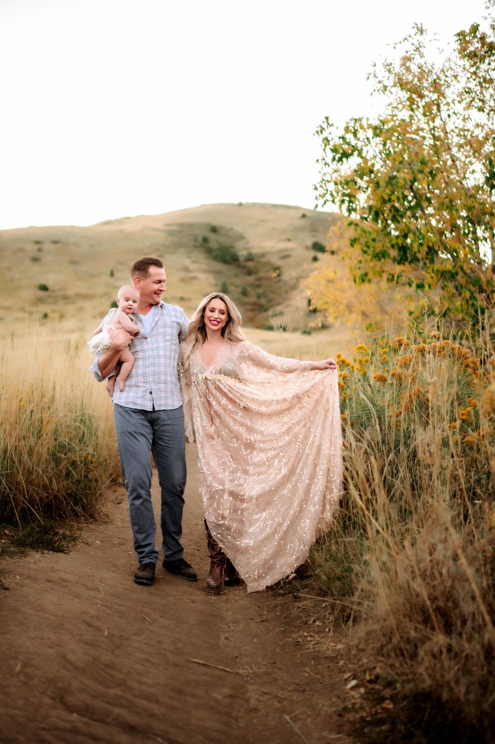 A couple walks on a dirt trail through autumn grass, with her flowing sparkly dress catching the light.