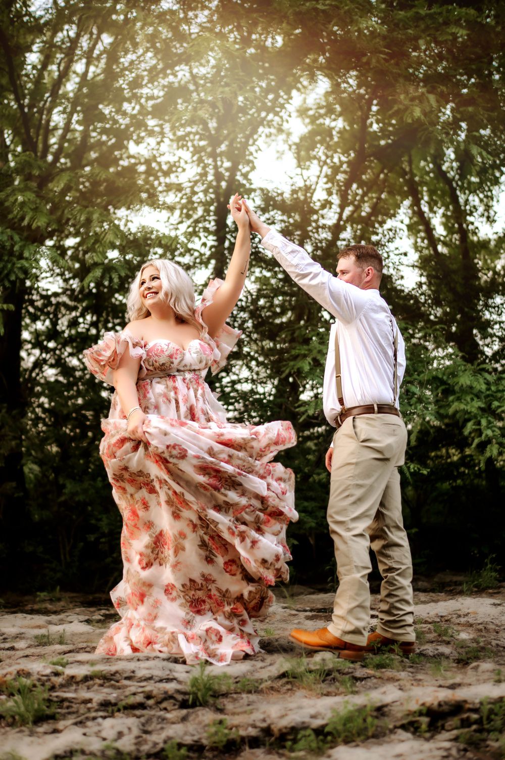 Couple dancing outdoors in formal wear with flowing floral dress and sunlit trees.