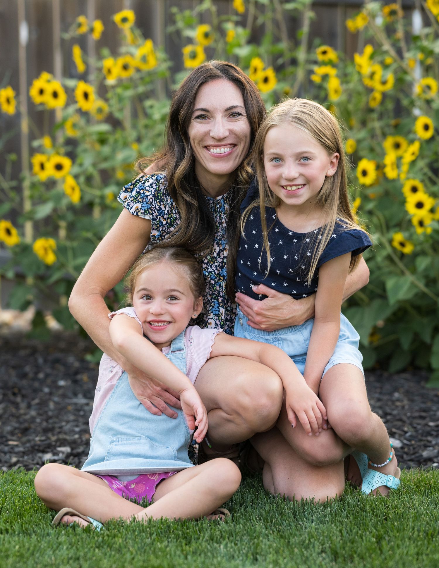A cheerful family portrait taken in front of blooming sunflowers in a garden.