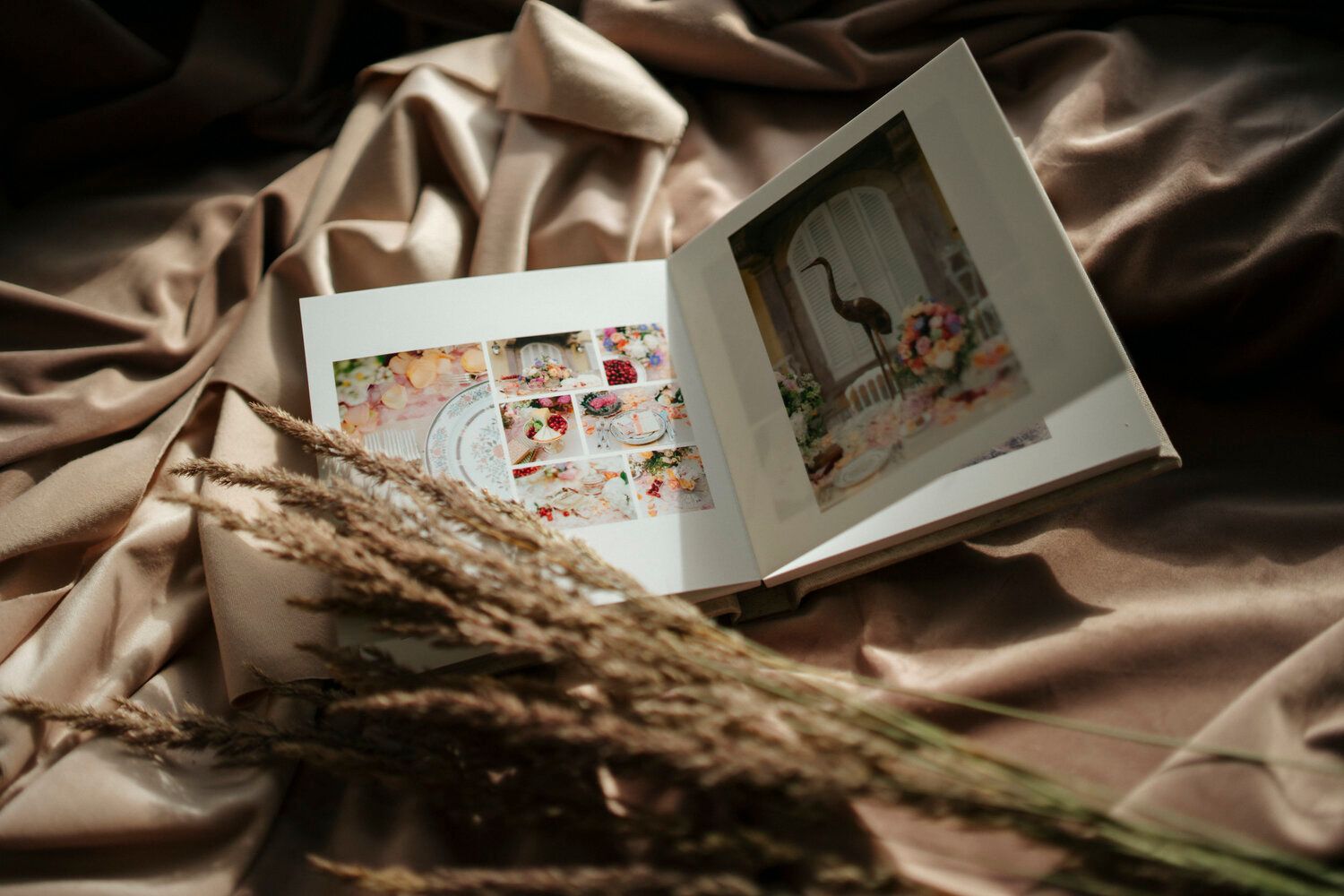 Open photo album displaying vintage photographs on silky fabric with dried flowers.