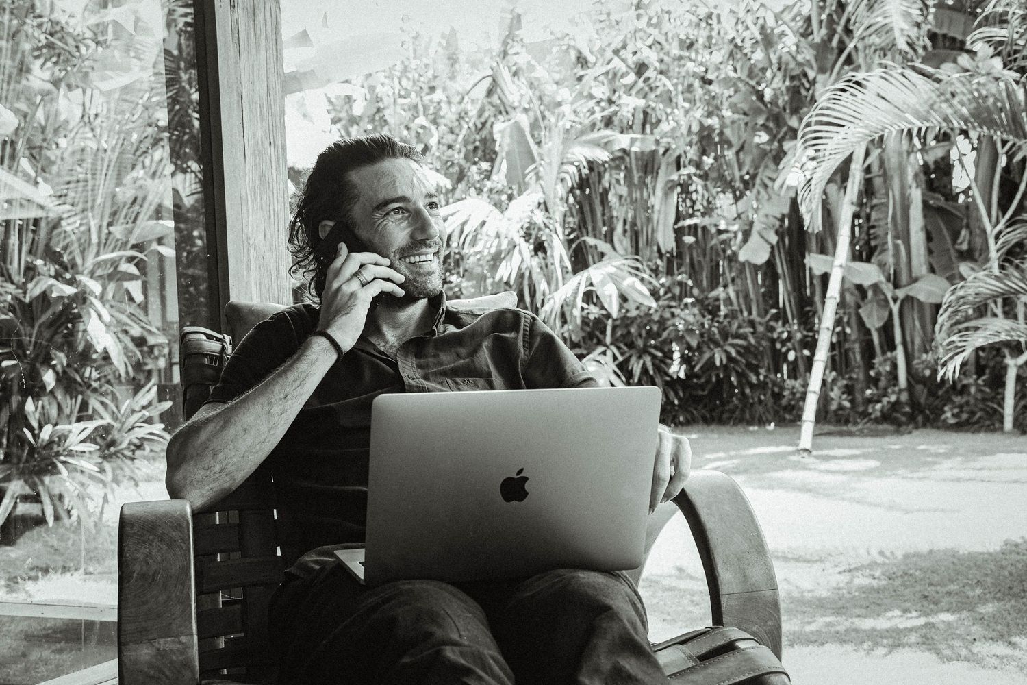 Person working on MacBook laptop outdoors with tropical garden in background.