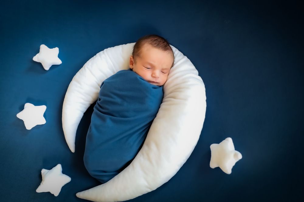 Newborn baby sleeping peacefully on dark blue background with white star decorations.