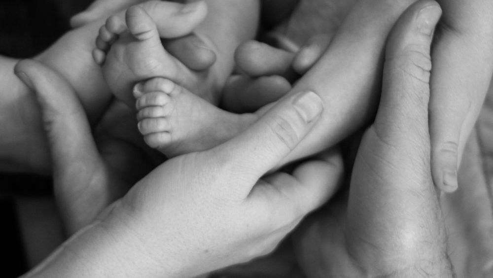 Close-up black and white image of gentle hands holding a newborn.