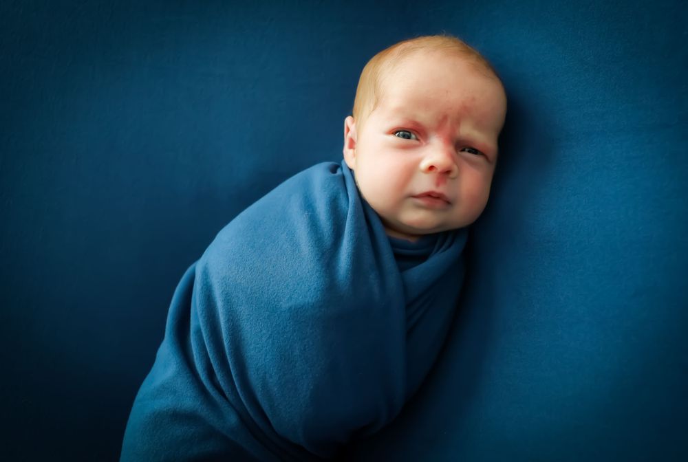 Baby portrait series showing peaceful sleeping expressions in blue wrap against navy background.