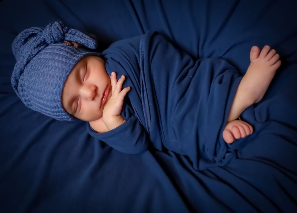 Baby in blue sleepwear resting on dark navy bedding with decorative elements.
