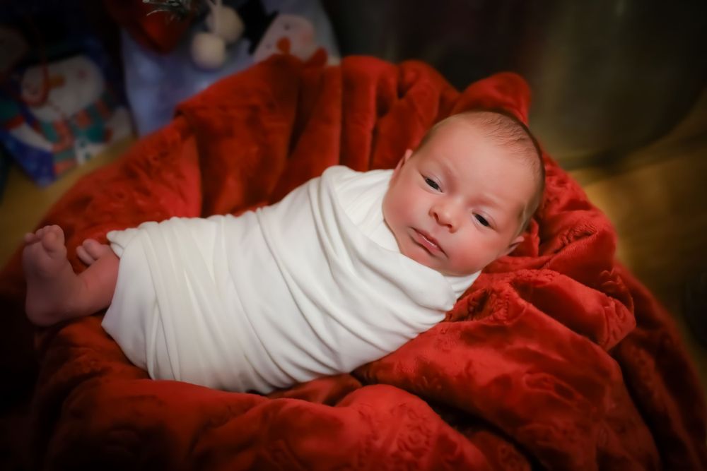 A newborn baby swaddled in white lying on red fabric in a series of photos.