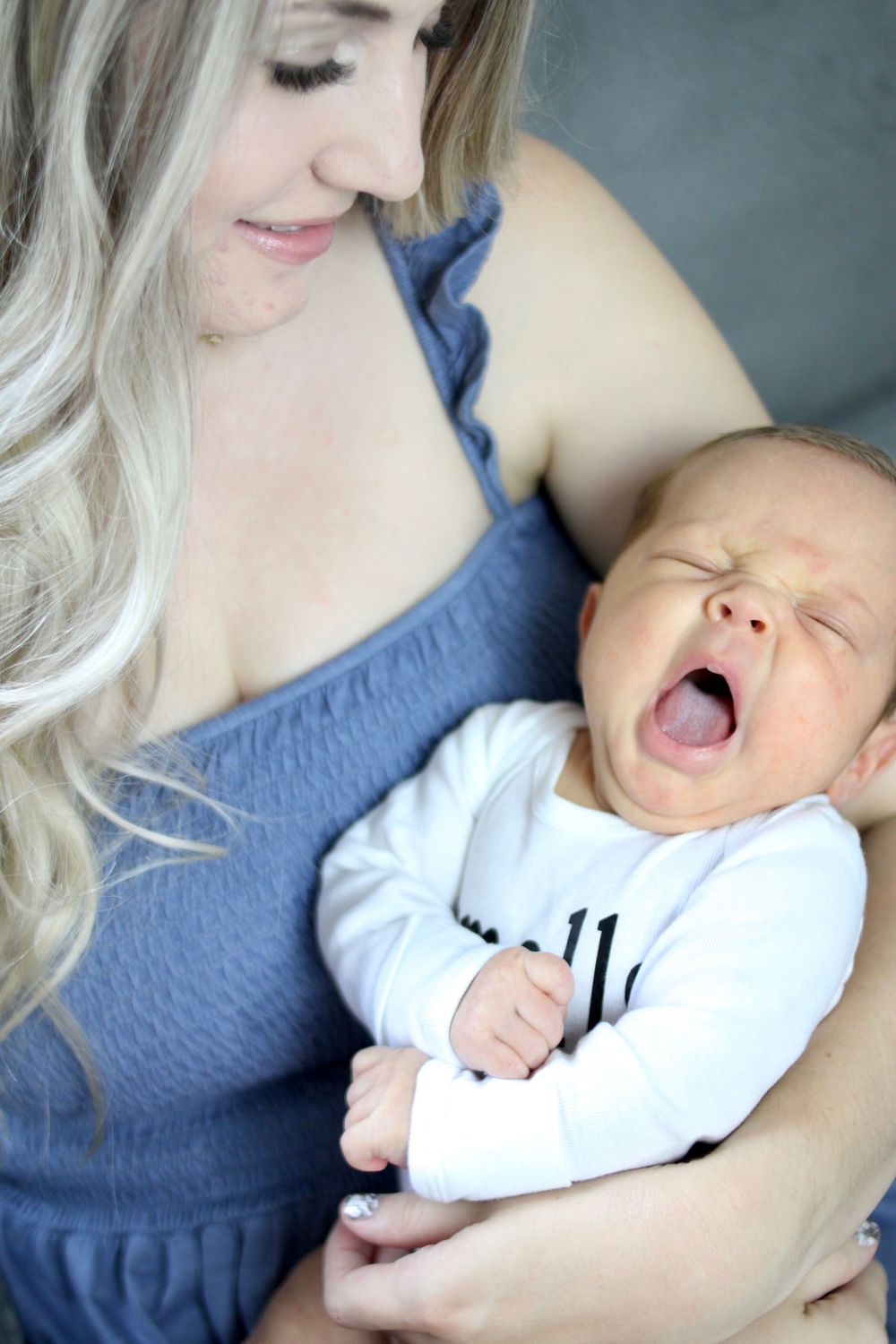 A sleeping infant in white clothing yawns while being held.