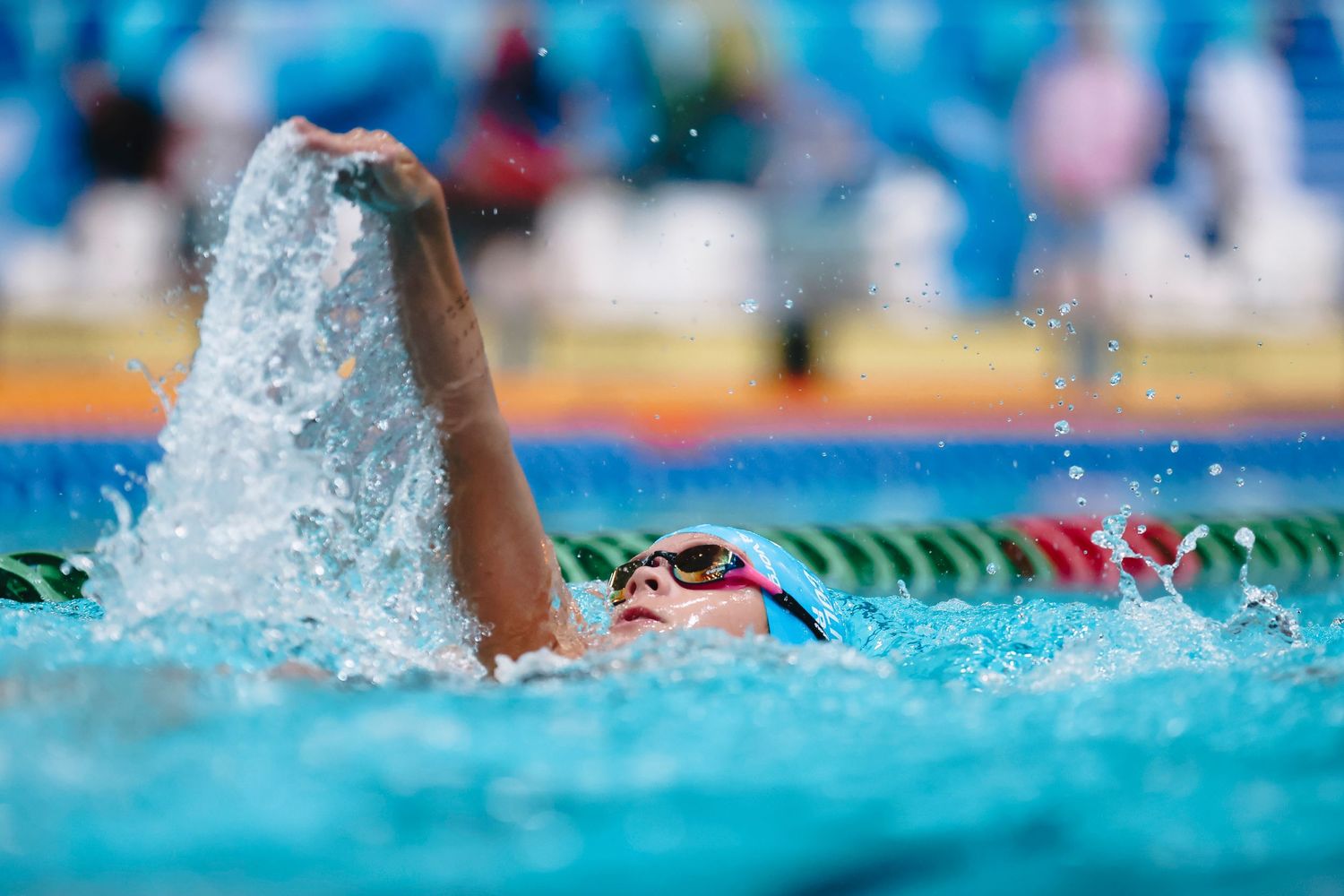 Competitive swimmer performs freestyle stroke during race with water splashing.