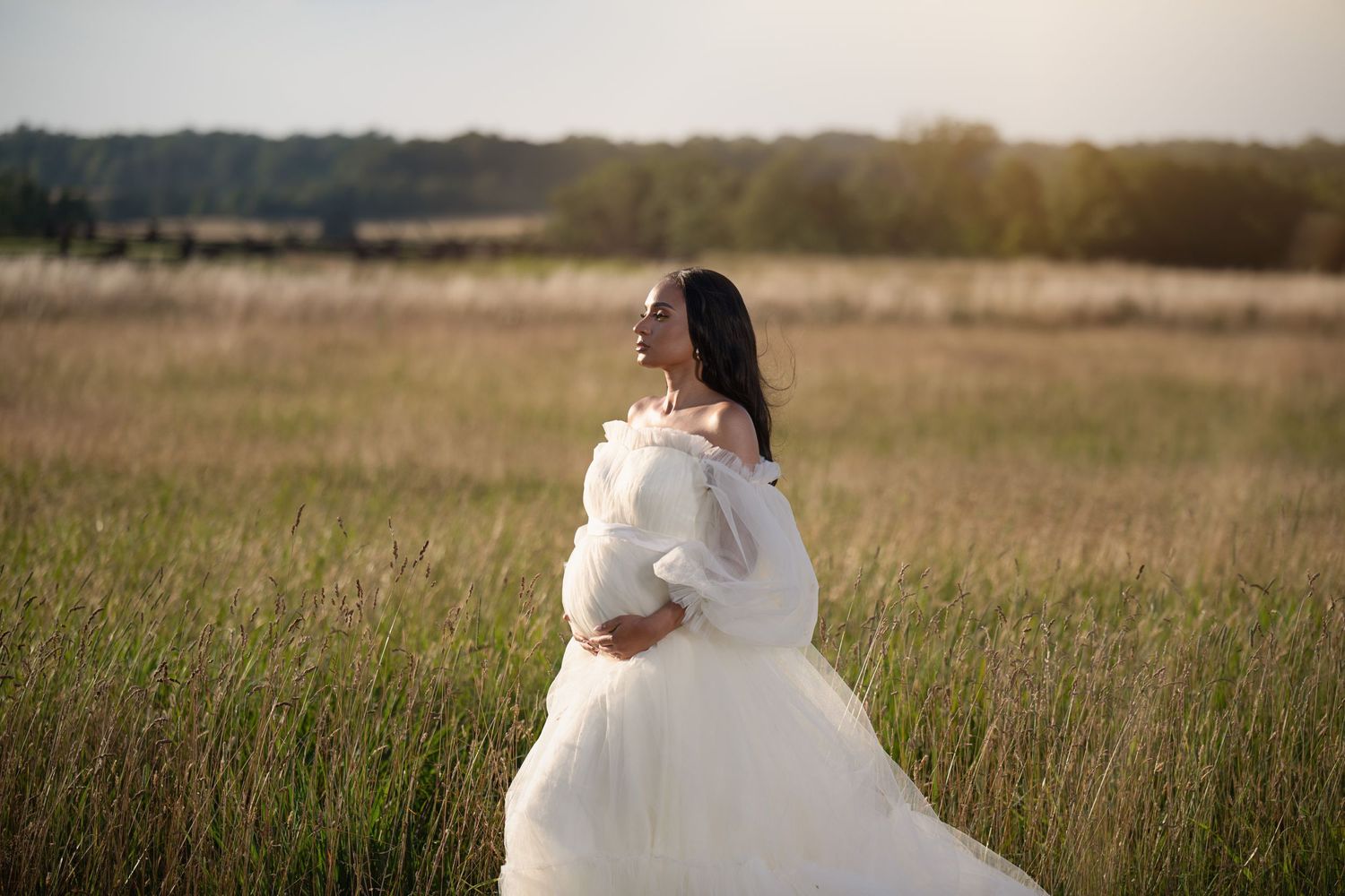 Ethereal bride in flowing white gown poses in golden field at sunset.