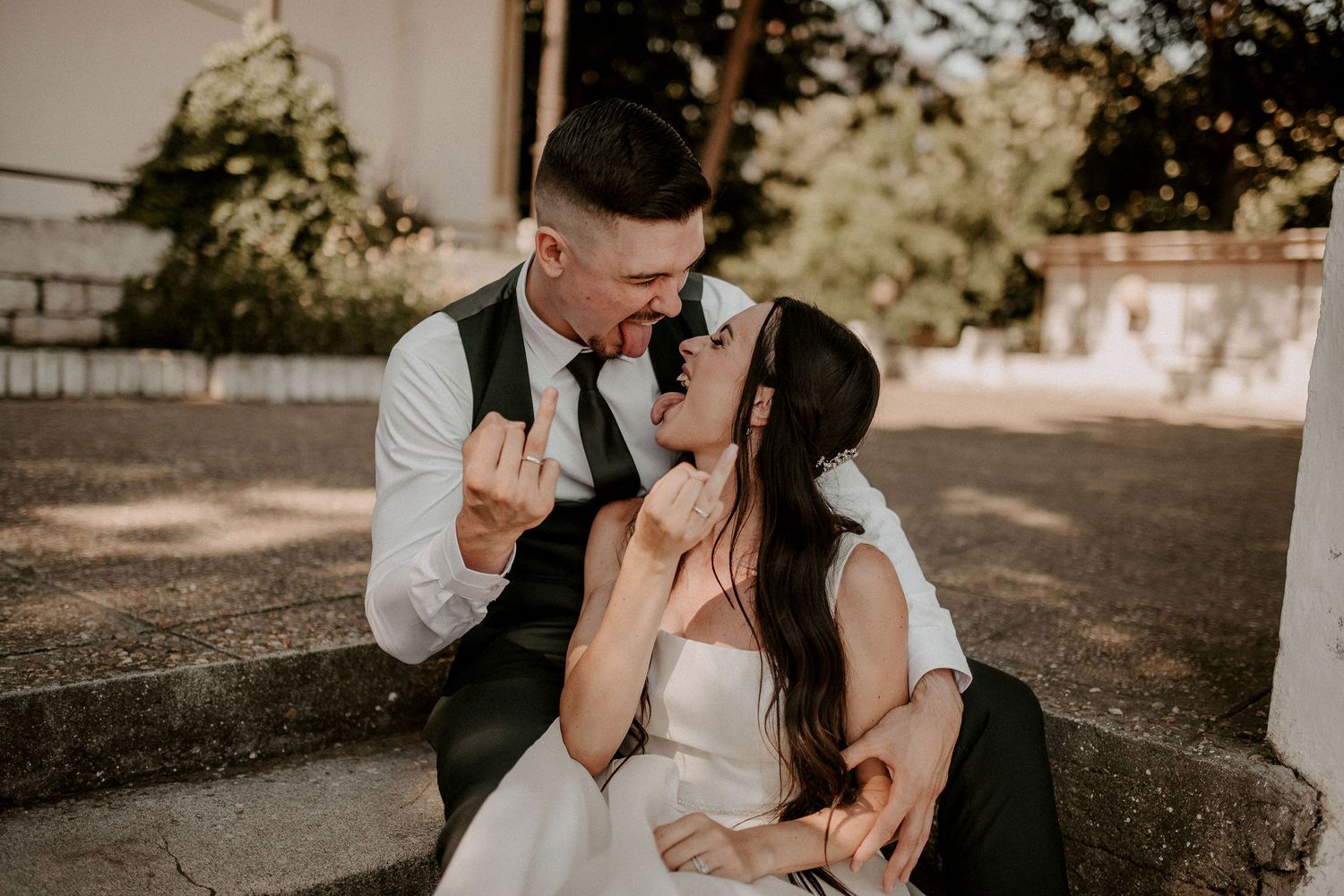 Wedding couple shares playful moment while sitting outdoors in casual attire.