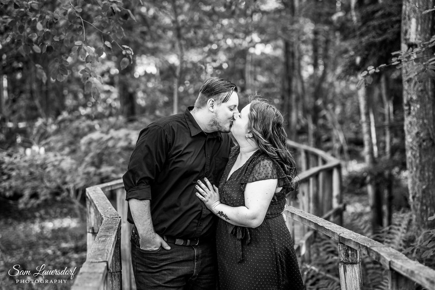 A romantic black and white portrait of a couple embracing on a wooden bridge in a forest setting. couples photography in wisconsin