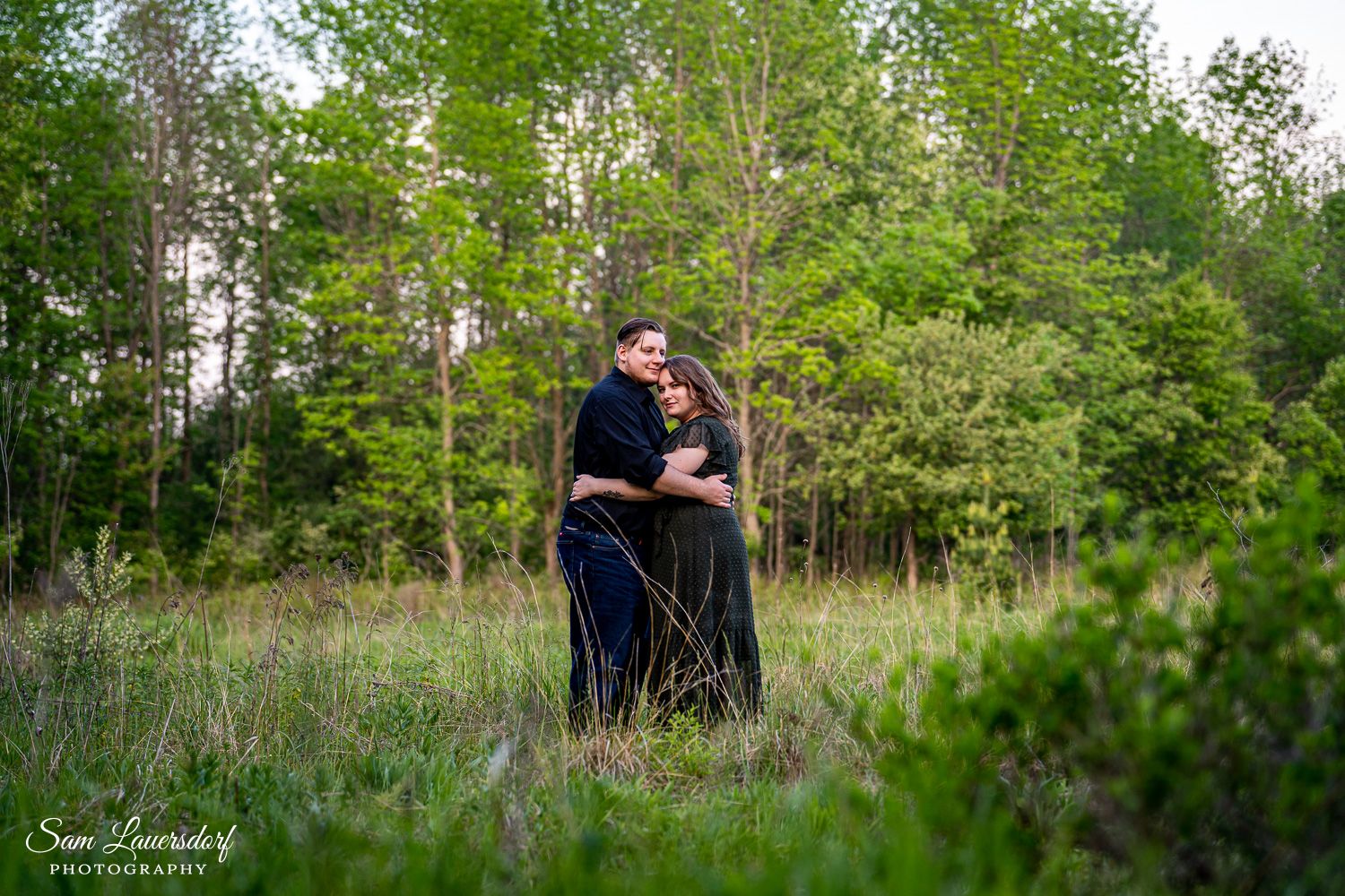 A couple embraces in a scenic meadow with spring trees and natural lighting. unique and creative couples photography in Wisconsin